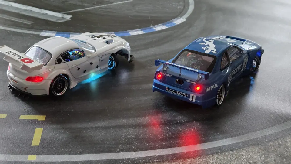 Zwei RC-Driftautos mit Beleuchtung auf einer grauen Driftstrecke
