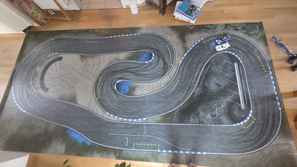 Draufsicht auf eine graue RC-Driftstrecke mit blauen Kurven und Fahrbahnmarkierungen