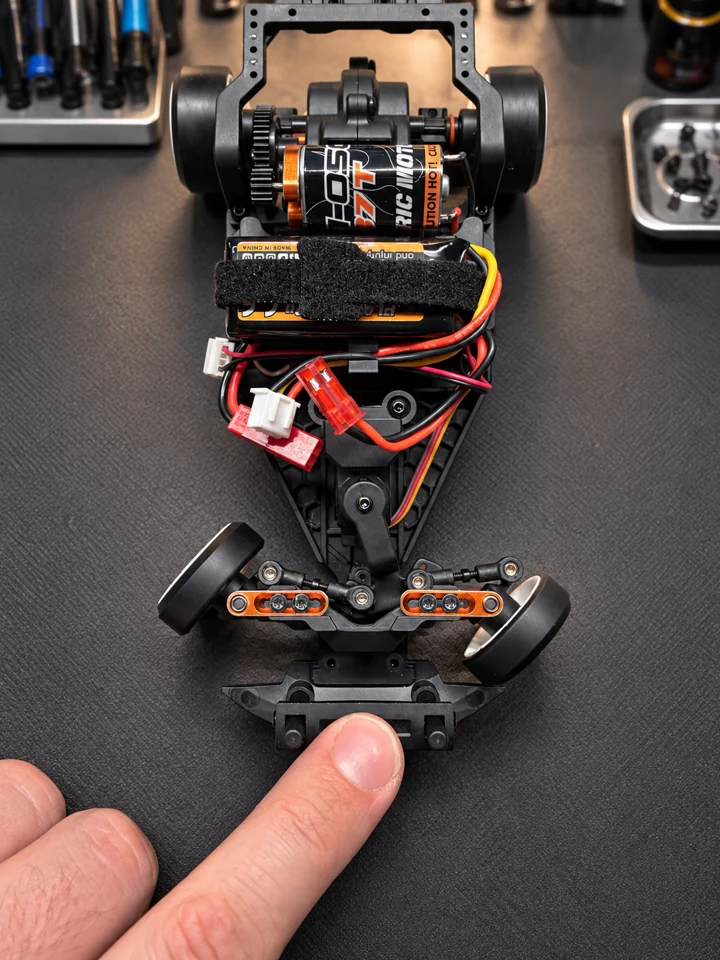 Top view of the HPI chassis with a finger pointing to the front steering mechanism