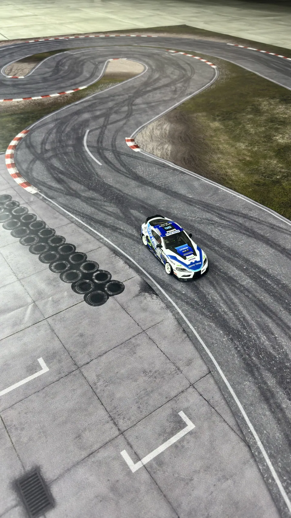 Blaues RC-Driftauto auf einer grauen Driftstrecke mit breiter Kurve